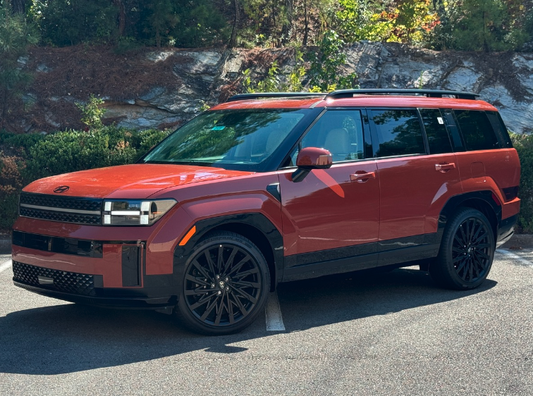 Red 2025 Hyundai SUV parked outdoors, surrounded by fall foliage and rocky terrain